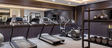 A modern gym with treadmills, elliptical machines, and a weight rack with dumbbells.