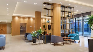 A modern lobby with a reception desk, seating area, and a large window offering a view of the city. - Courtyard by Marriott Tashkent (Tashkent)