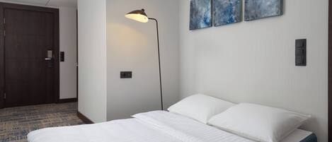 A hotel room with a bed, a floor lamp, and two abstract paintings on the wall.