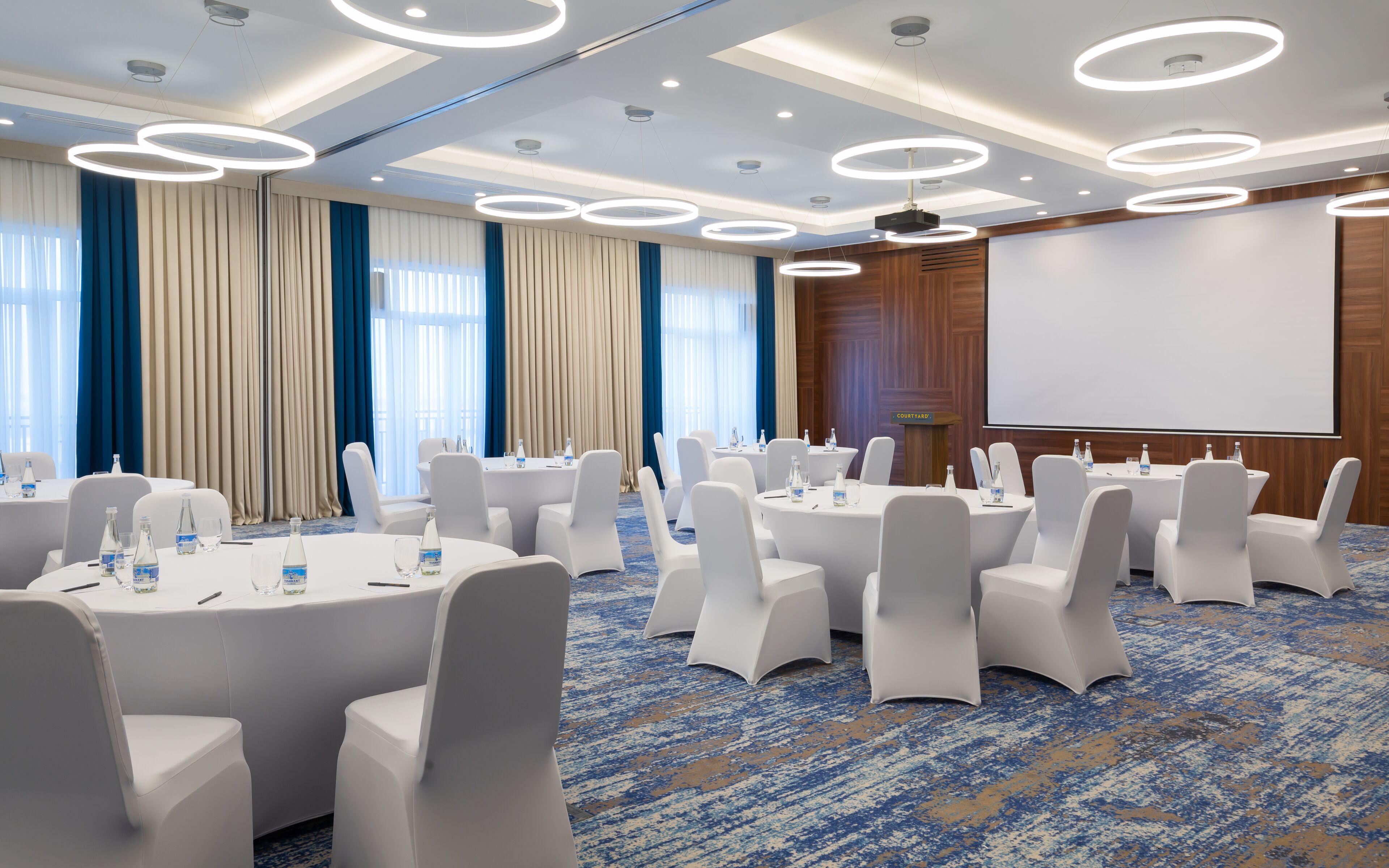 A conference room with round tables, white chairs, and a large screen.