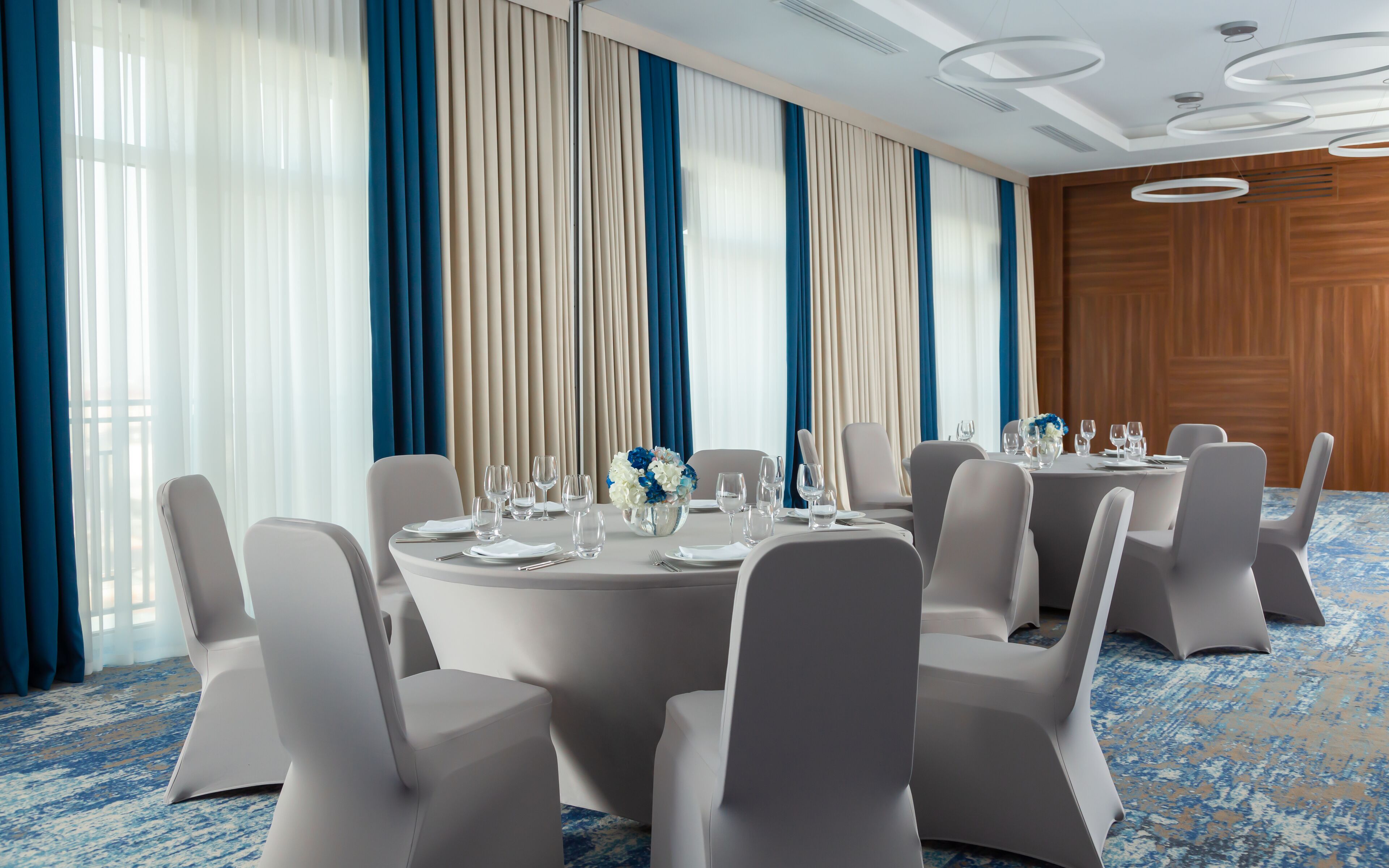 A conference room with round tables, white chairs, and a blue and beige color scheme.