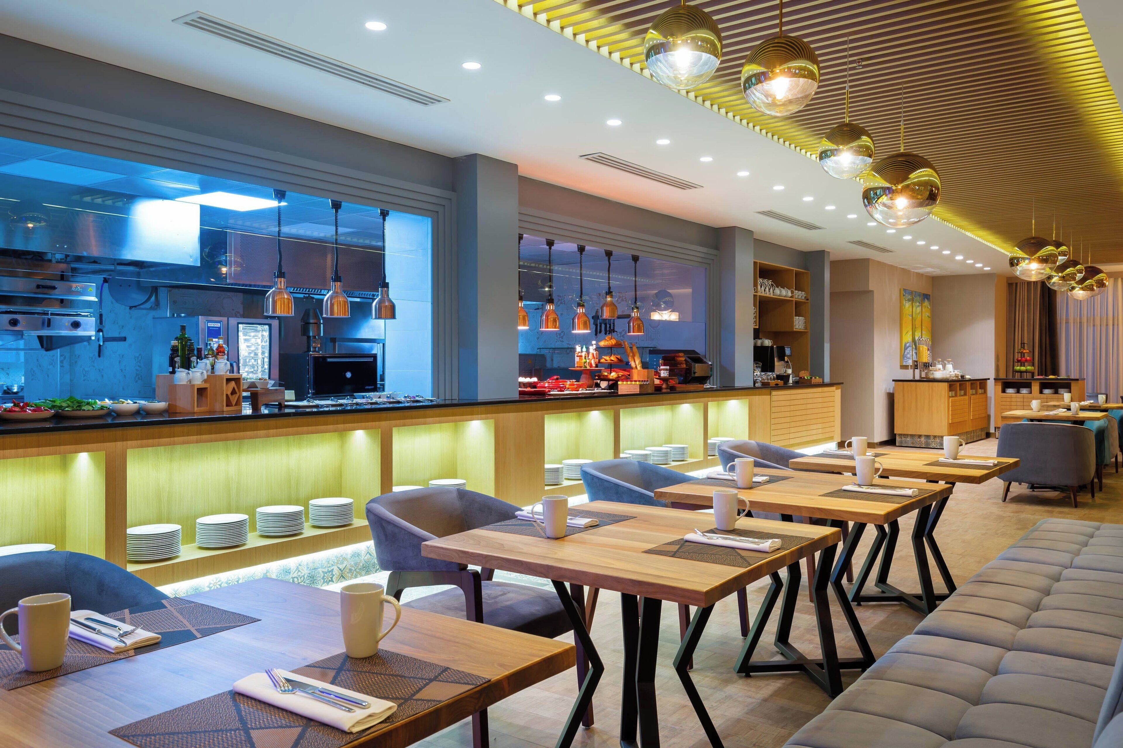 A modern restaurant with a bar area, seating with tables and chairs, and a kitchen in the background.