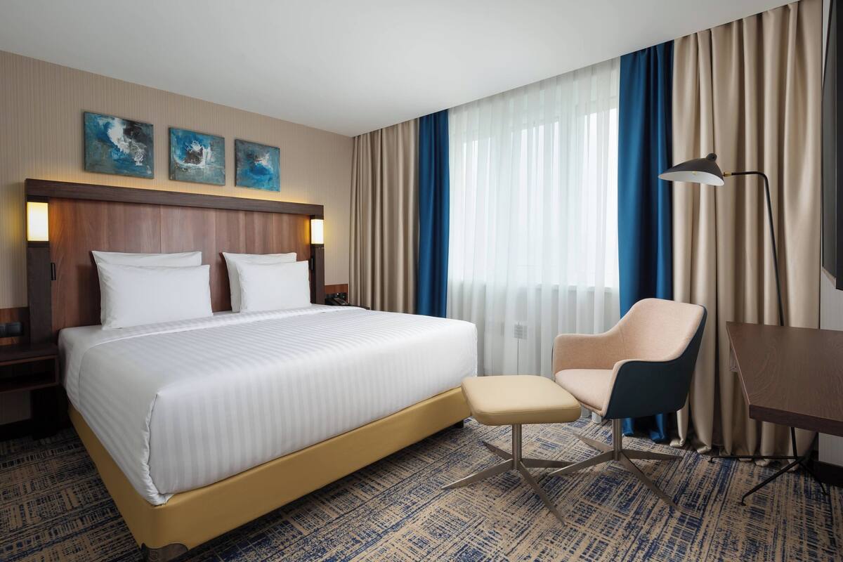 A hotel room with a large bed, a desk, a chair, and a nightstand.