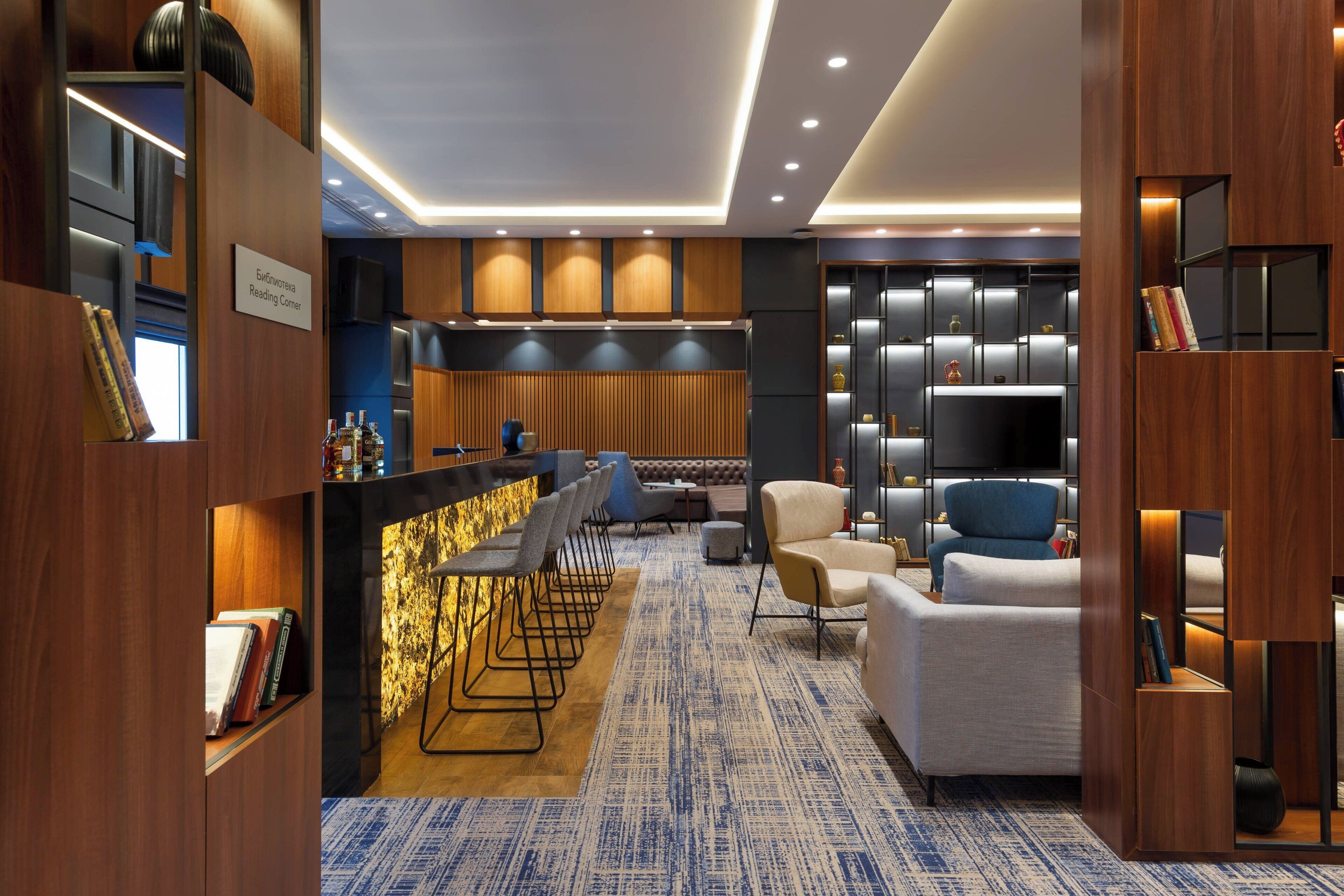 A modern hotel lobby with a bar area, seating, and a television.