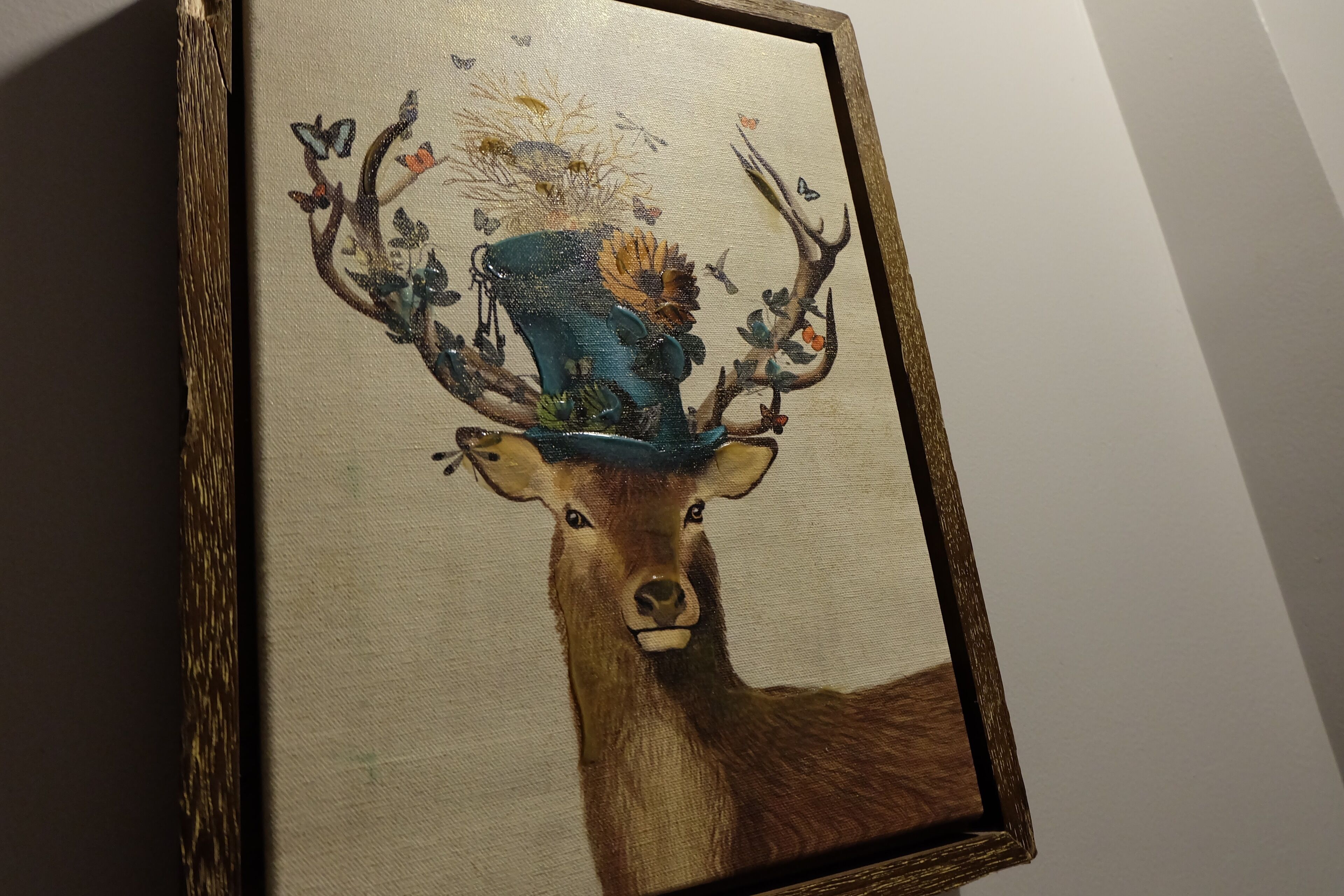 Een lijstwerk met een schilderij van een hert met een blauwe hoed en takken.
