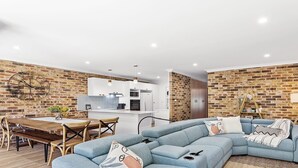 Una sala de estar moderna con un sofá seccional, una mesa de comedor con sillas y una cocina al fondo.