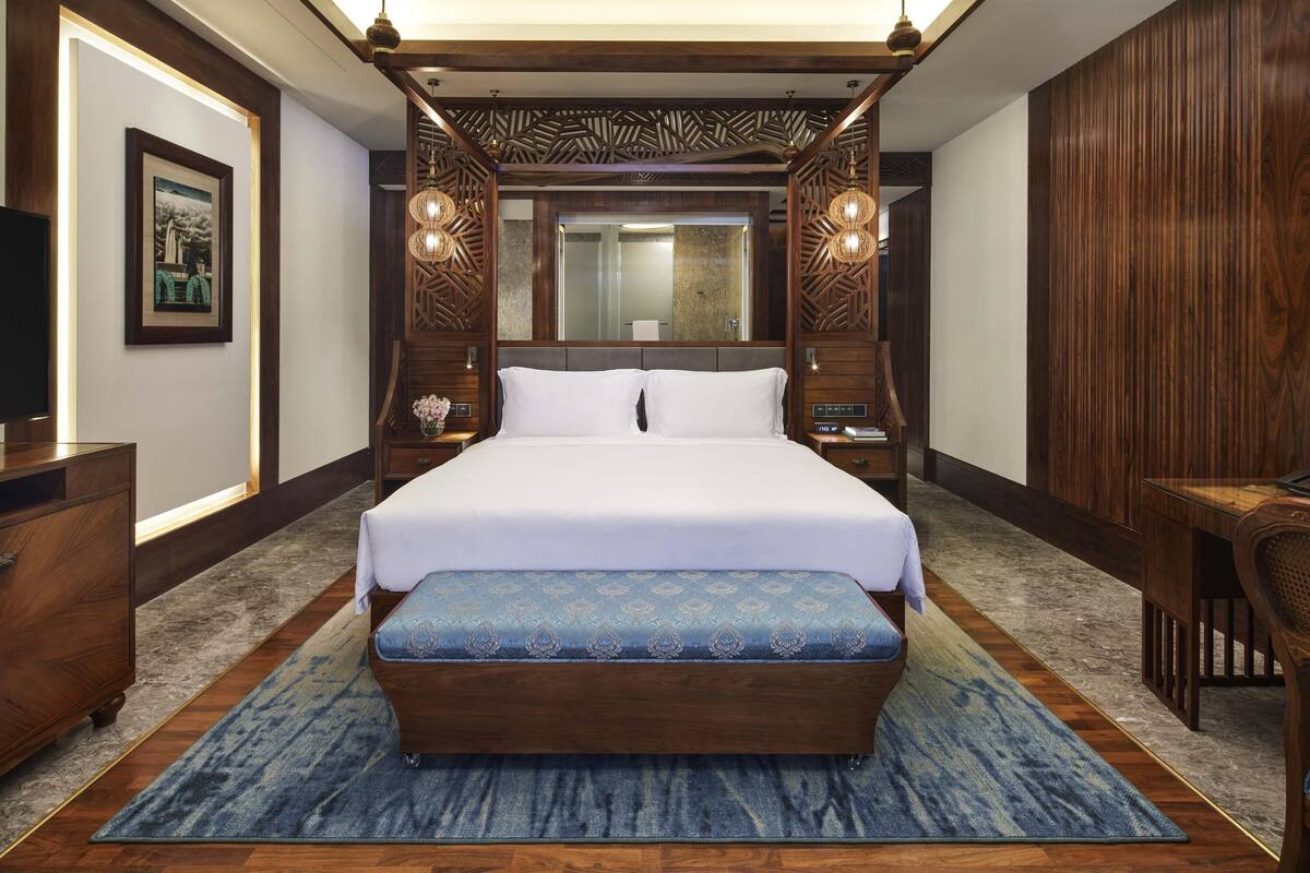 A spacious bedroom with a large bed, a wooden headboard, a bedside table, a nightstand, a mirror, and a wooden panel wall.