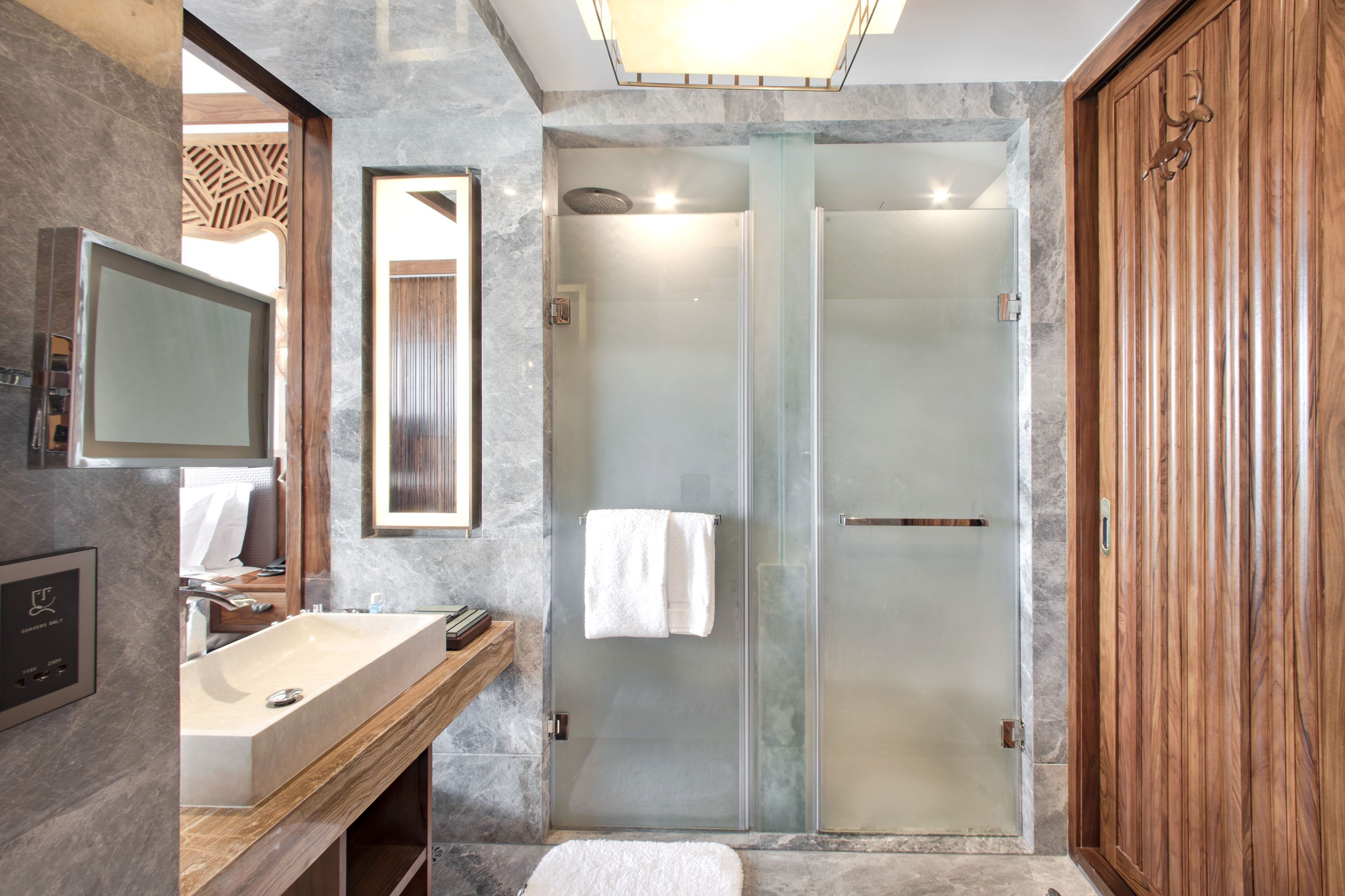A modern bathroom with a marble sink, a glass-enclosed shower, and a wooden vanity.