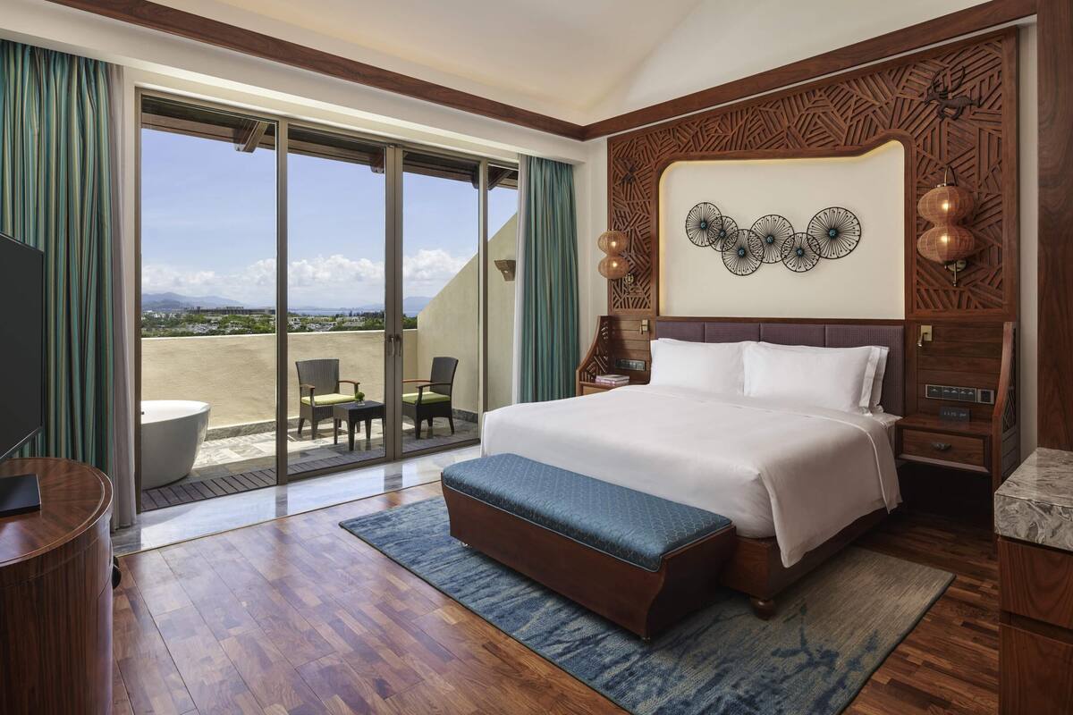 A spacious bedroom with a large bed, a balcony with a view, and a TV.