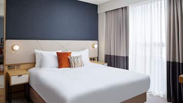 Habitación de hotel con una cama grande, dos mesitas de noche y un ventanal con cortinas.