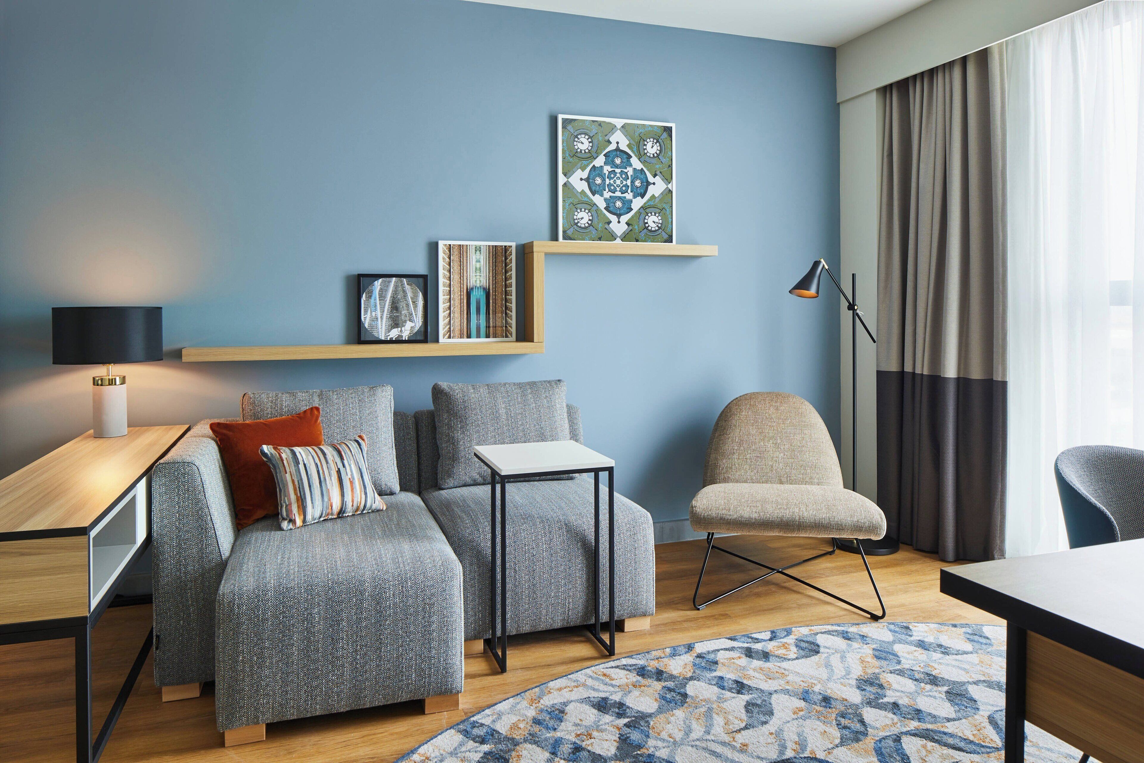 A modern living room with a grey sofa, a small side table, a chair, and a large window with curtains.