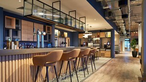 Un bar moderno con una barra larga, varios taburetes y una amplia variedad de botellas y copas.