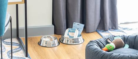Ein Bereich für Haustiere mit zwei Metallnäpfen, einem weichen Entenspielzeug und einem Futtersack für Hunde auf dem Boden.