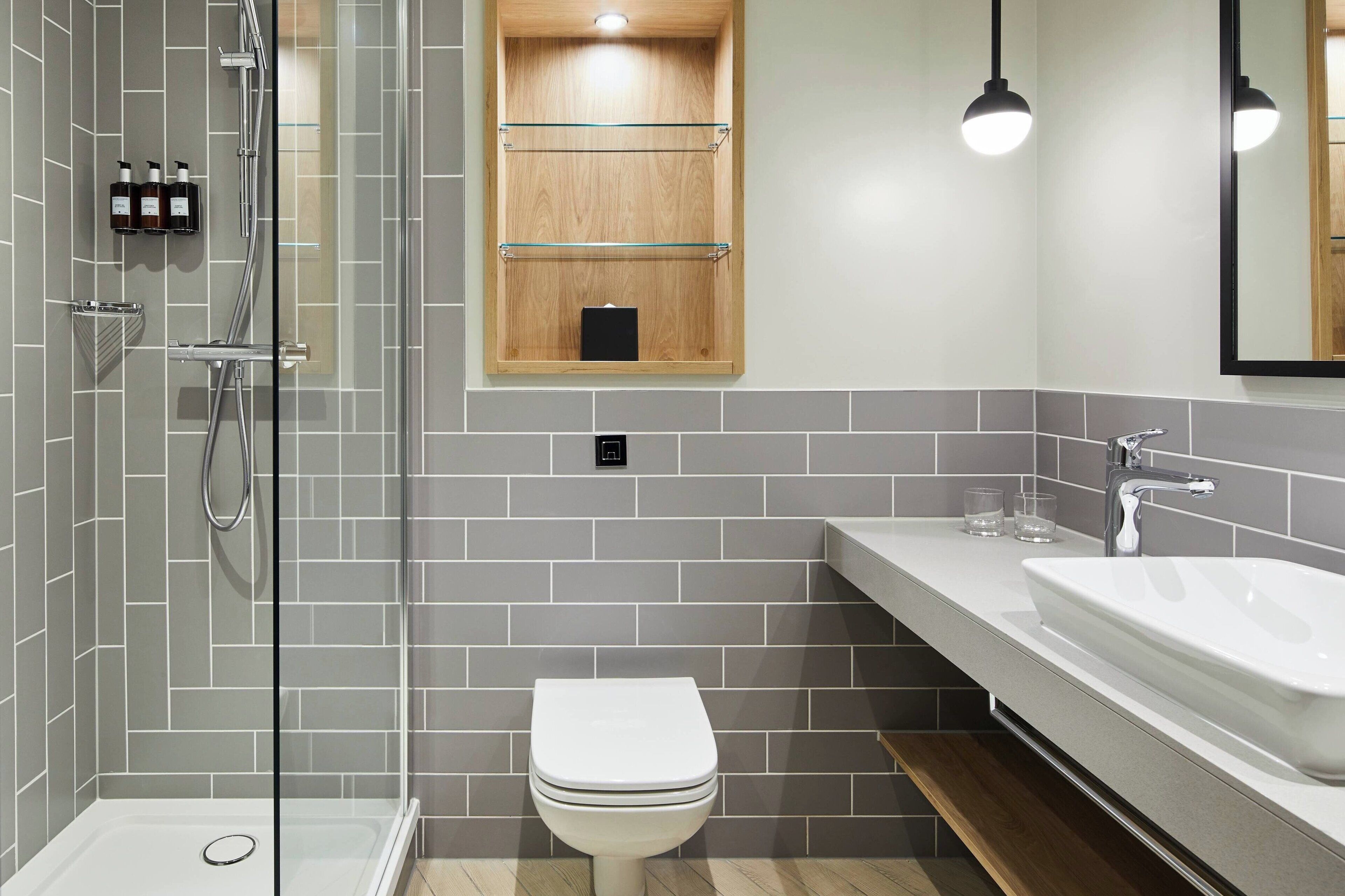 Une salle de bain moderne avec une douche à parois de verre, des toilettes blanches, un meuble à pharmacie en bois et un grand lavabo avec un miroir au-dessus.