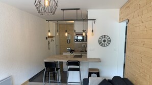 Ein modernes Wohnzimmer mit einem dunkelgrauen Sofa, einem Holztisch und einer Küchenzeile im Hintergrund.
