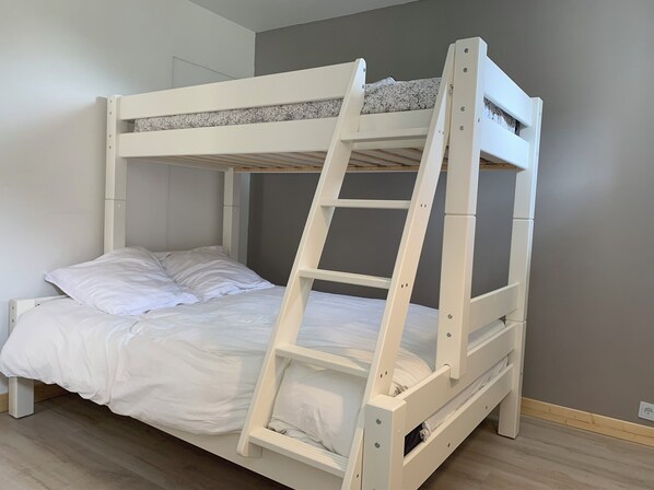 A bunk bed with a ladder, white bedding, and a grey wall.