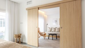 Une chambre moderne avec un grand lit, une armoire en bois, un petit tabouret et un canapé avec une lampe.