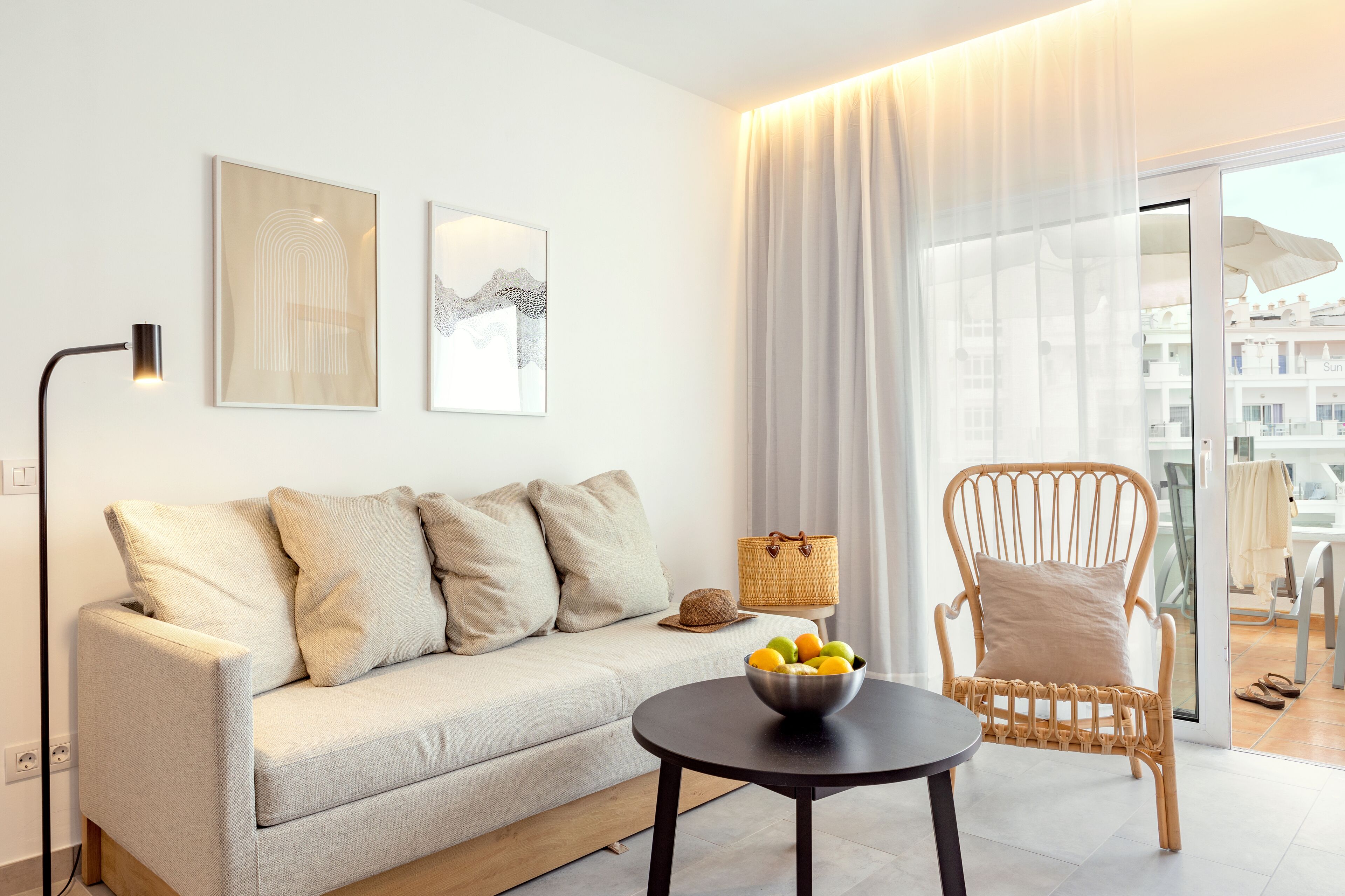 A modern living room with a sofa, a wicker chair, a table with fruit, and artwork on the wall.