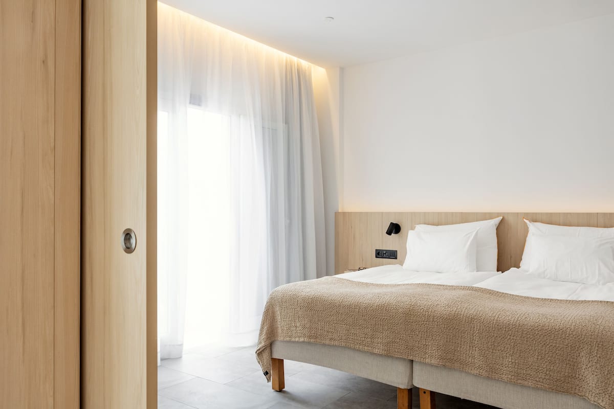 Una habitación de hotel moderna con una cama grande, una puerta de madera y vistas a través de una cortina translúcida.