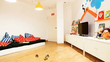 A children's play area with a sofa, toys, a television, and a brick wall decoration.