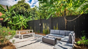 Une terrasse avec un canapé gris, un banc en bois et une table.