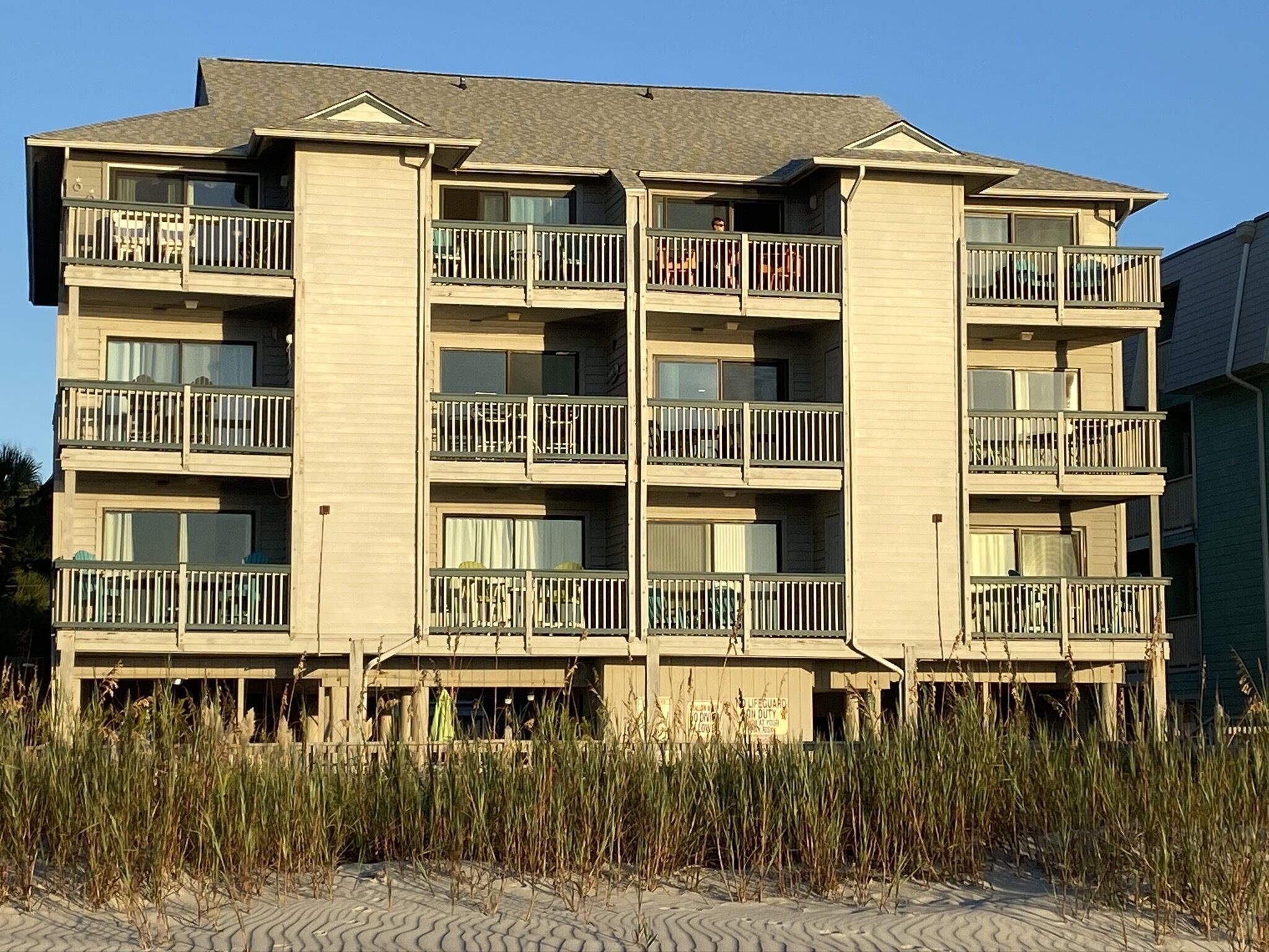 A multi-story building with balconies, a lifeguard duty sign, and a sandy ground.