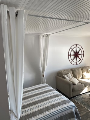 Ein Schlafzimmer mit einem Bett, einem Schlafsofa, einer Wanddekoration mit Kompass und einer Decke mit Gittermuster.