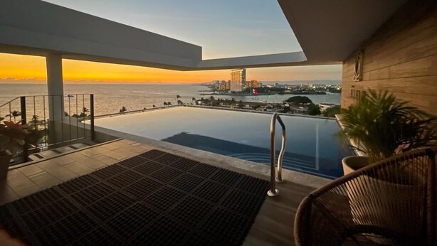 A modern balcony with a view of the sea and city skyline at sunset.