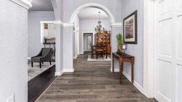 A hallway with a wooden floor, white walls, and a dining area in the background.