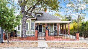 A two-story house with a front porch, brick columns, and a black metal fence.