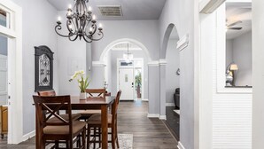 A dining area with a wooden table and chairs, a chandelier, and a white archway leading to another room.