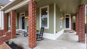 A house with a green exterior, brick columns, and a porch with two rocking chairs.