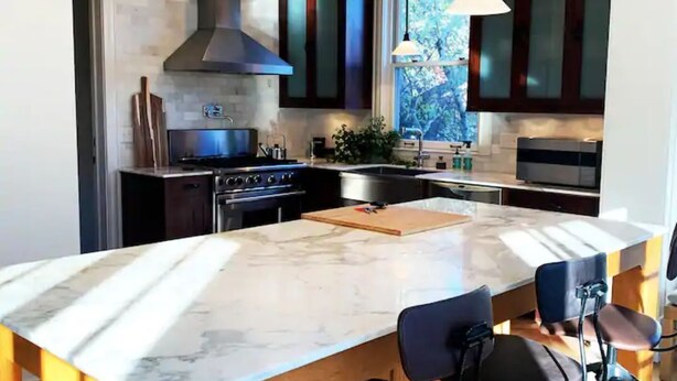 A modern kitchen with a large island, dark cabinetry, and pendant lighting.