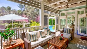 A covered outdoor seating area with a sofa, tables, and a view of a pool and garden. - WaterColor - 4+BR, Private Heated Pool, 6 Seat LSV - 6 Bikes (Santa Rosa Beach)