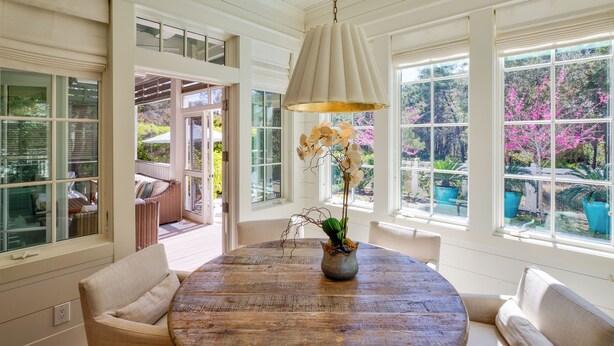 A round wooden table with a vase of flowers, white upholstered chairs, and a hanging light fixture in a room with large windows and white walls. - WaterColor - 4+BR, Private Heated Pool, 6 Seat LSV - 6 Bikes (Santa Rosa Beach)