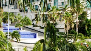 A modern building with multiple balconies, a pool area, and lush palm trees. - Coco Room 2 by B&G - Cancún Hotel Zone (Cancún)