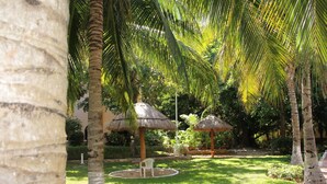 A tropical garden with palm trees, thatched-roof structures, and a circular seating area. - Coco Room 2 by B&G - Cancún Hotel Zone (Cancún)