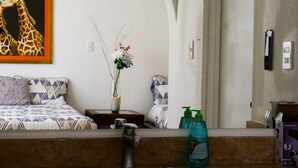 A bathroom with a bed, a painting of giraffes, a vase with flowers, and toiletries. - Coco Room 2 by B&G - Cancún Hotel Zone (Cancún)