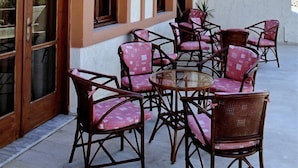 An outdoor seating area with wicker chairs and a glass table, adjacent to a building with arched windows and a balcony. - Anatoli Apartments (Hersonissos)
