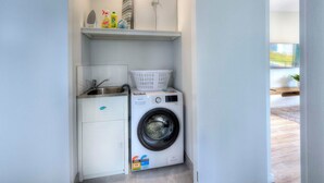 A compact laundry area with a washing machine, a sink, and a small cabinet. - Archella 2 - Freycinet Holiday Houses (Coles Bay)