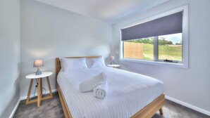 A bedroom with a bed, two bedside tables, a window with a view of the outdoors, and a ceiling light. - Archella 2 - Freycinet Holiday Houses (Coles Bay)