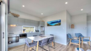 A modern kitchen with grey cabinets, a white countertop, and a dining area with a white table and grey chairs. - Archella 2 - Freycinet Holiday Houses (Coles Bay)