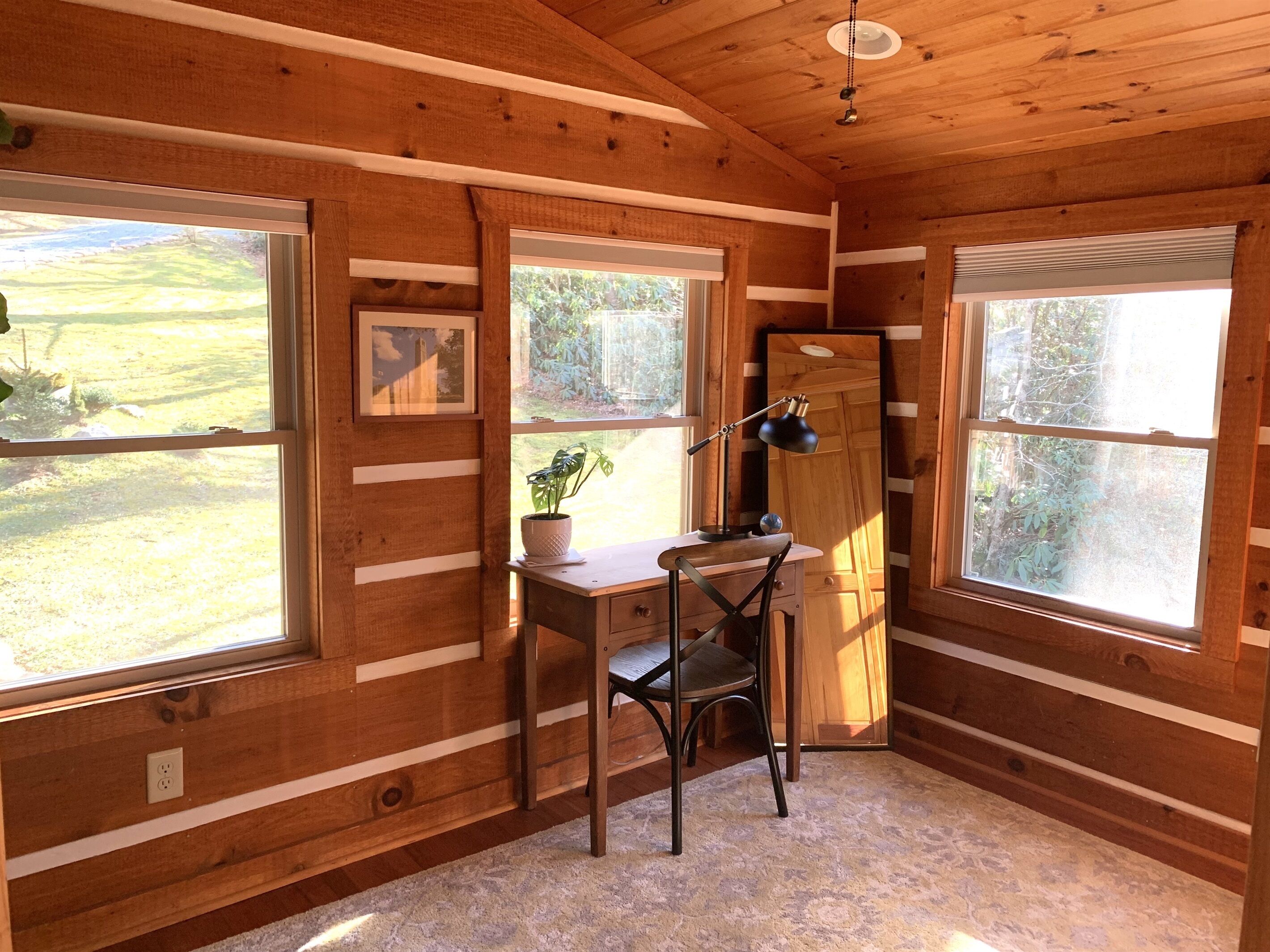 Una habitación de cabaña de madera con escritorio, silla y ventanas amplias.