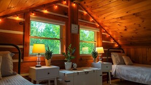 Une chambre confortable de style cabane, avec deux lits, des murs en bois, de grandes fenêtres et des guirlandes lumineuses.