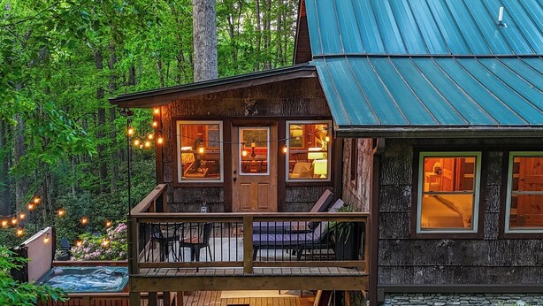 Un chalet rustique doté d’une terrasse en bois, d’un bain à remous et de guirlandes lumineuses.