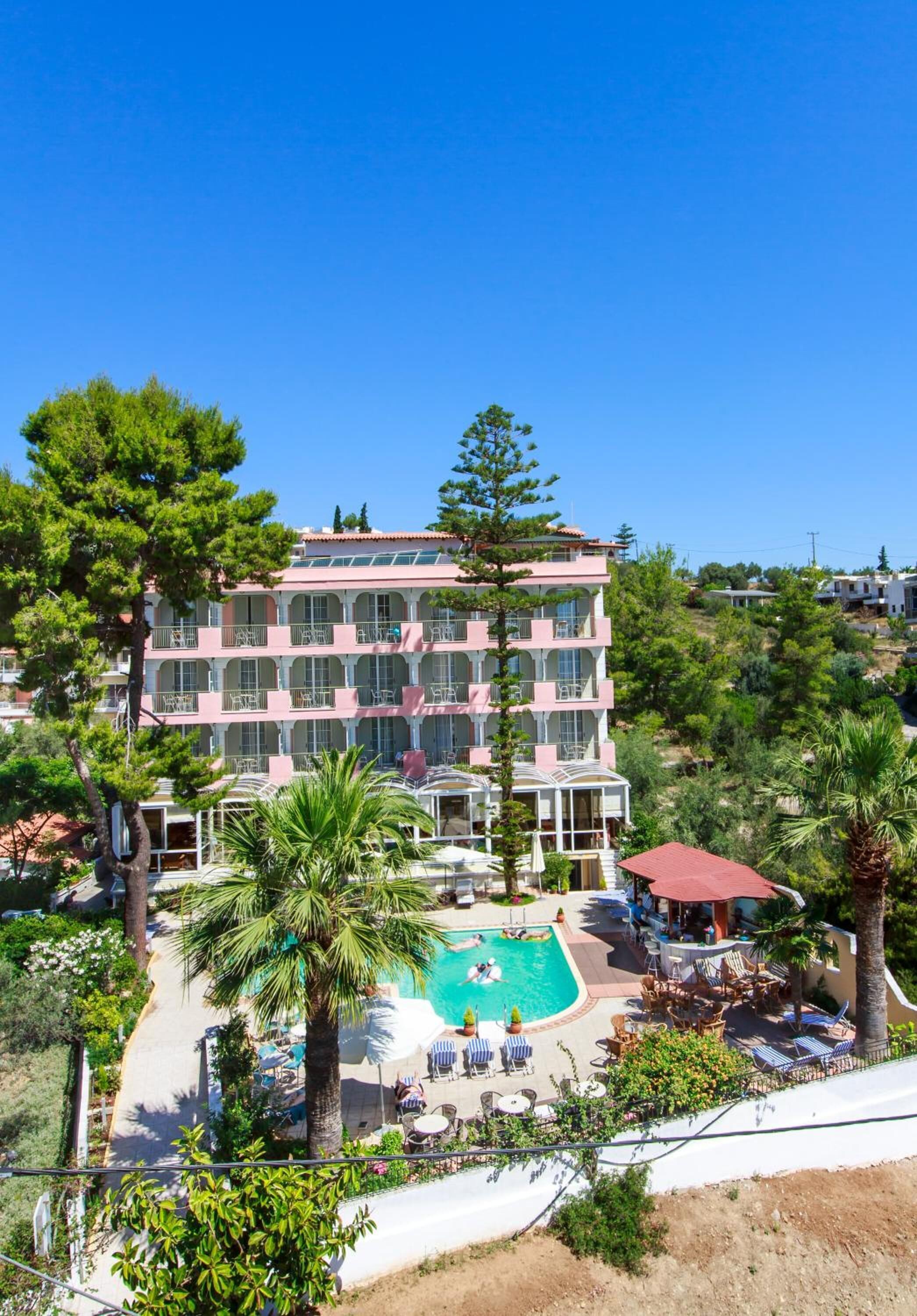 A multi-story hotel with a pool area, outdoor seating, and lush greenery.