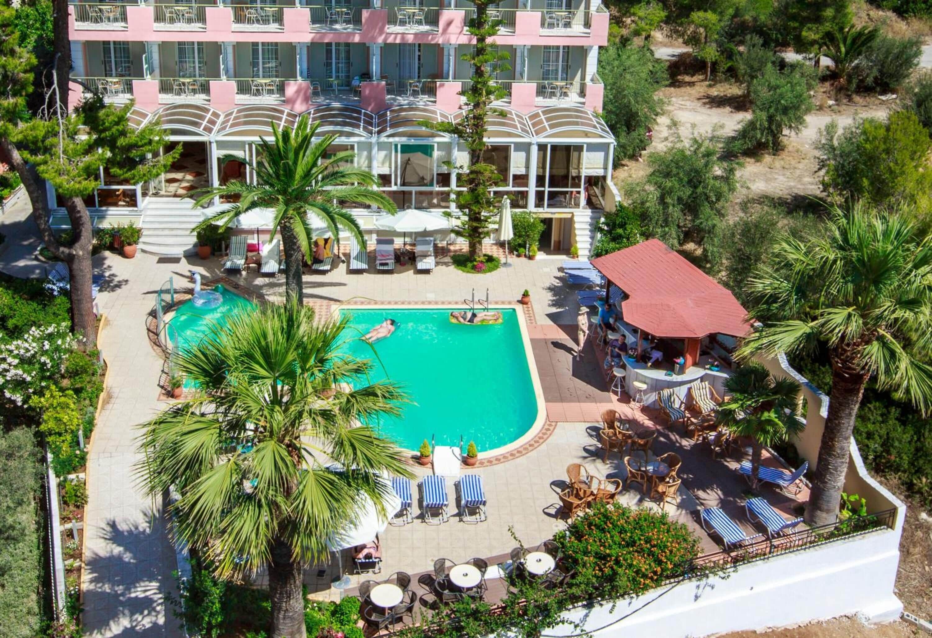 A multi-story hotel with a swimming pool surrounded by palm trees and sun loungers.