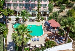 A multi-story hotel with a swimming pool surrounded by palm trees and sun loungers.