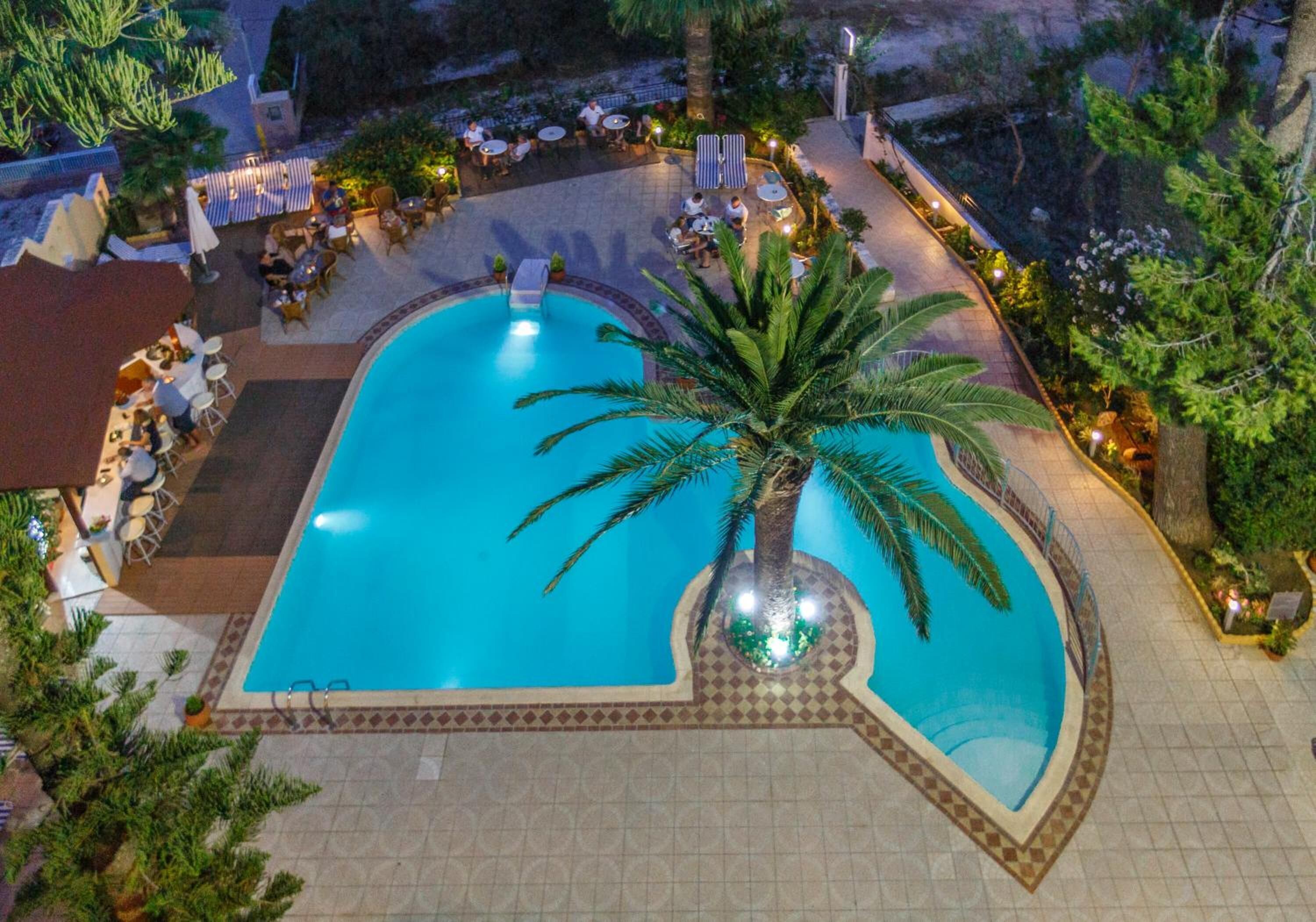 A swimming pool with a palm tree in the center, surrounded by lounge chairs and tables.