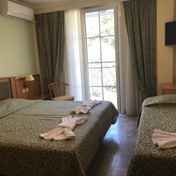 A hotel room with two beds, a chair, a desk with a lamp, and a large window with curtains. - Tolon Holidays (Nafplio)